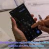 Pessoa segurando um smartphone com a calculadora aberta na tela, digitando com o dedo sobre recibos e faturas na mesa.