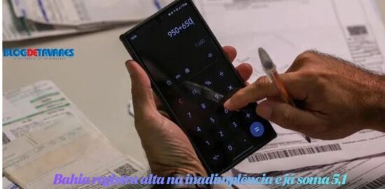 Pessoa segurando um smartphone com a calculadora aberta na tela, digitando com o dedo sobre recibos e faturas na mesa.