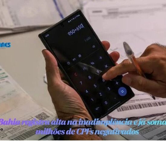 Pessoa segurando um smartphone com a calculadora aberta na tela, digitando com o dedo sobre recibos e faturas na mesa.