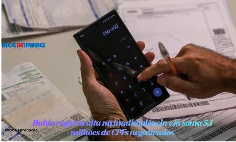 Pessoa segurando um smartphone com a calculadora aberta na tela, digitando com o dedo sobre recibos e faturas na mesa.