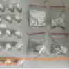 Seized items on a gray table: white bags with powders and small plastic containers, with an orange news caption about cocaine arrest in Portuguese.